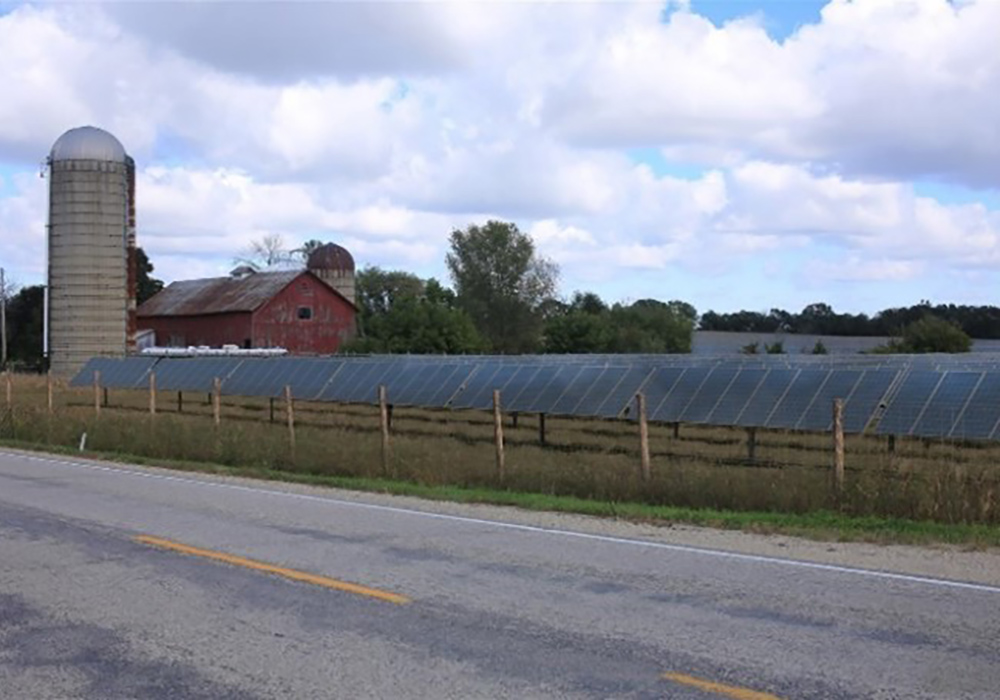 PV arrays behind a rustic fence along a rural road.