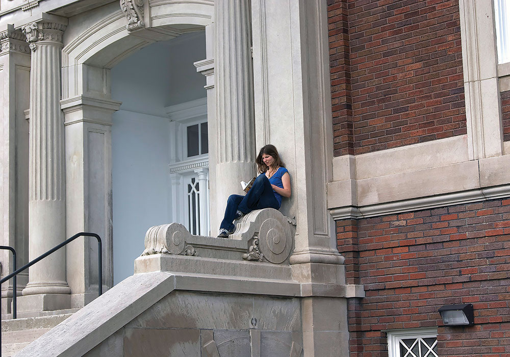 A young woman reading on the grand staircase of Stoddard Johnston Scholar House. Photo courtesy Family Scholar House.