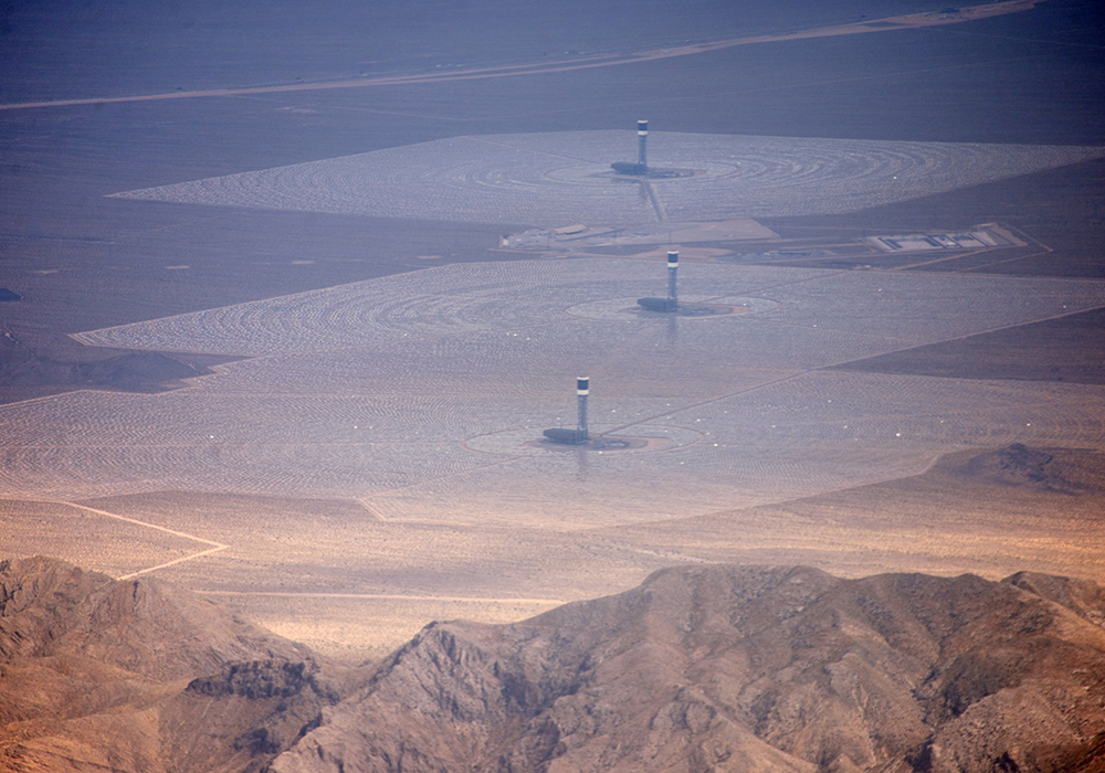 Three tall towers in a desert, each surrounded by thousands of solar collecting mirrors.